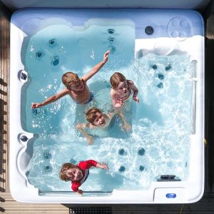 Four children stare up at the camera from within a white hot tub with clear blue water.