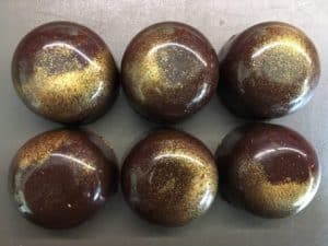 Six round chocolate balls with a glossy, gold glitter coating.