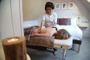 A woman lays on her stomach and receives a back massage as a candle burns in the foreground.