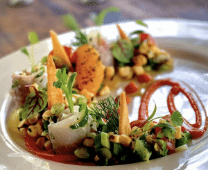 A white plate containing green salad and herbs is accompanied by grains and roasted sliced vegetables.