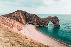 Lulworth's Durdle Door. A rock archway emerges from a blue sea, next to a sandy beach and grassy cliffs.