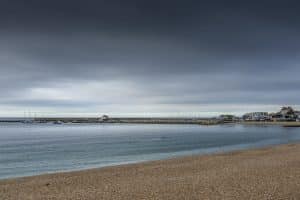 A dark blue-grey sky overlooks a calm, blue sea and empty beach.