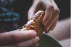 A closeup of a child's hands, holding a melted marshmallow between two biscuits.