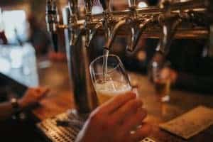 A closeup of silver bar taps, as a bartender pours a glass of beer inside a pub.