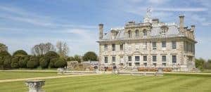 Kingston Lacy, a National Trust stately home, has a grey exterior with Venetian architecture, surrounded by a freshly-cut lawn, under a blue sky.