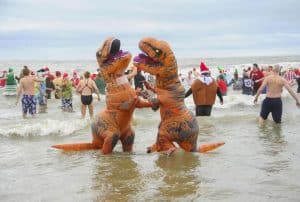 Two people dressed as dinosaurs in the sea at Charmouth, Dorset