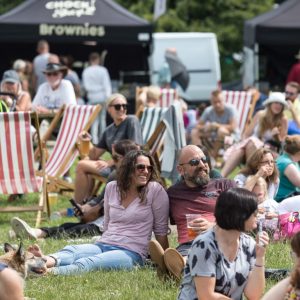 People sat smiling, wearing sunglasses, on grass and stripy deckchairs at Weymouth Food Festival
