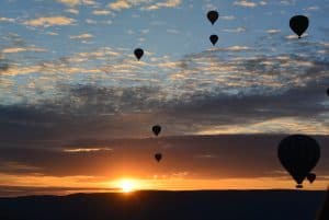 Eight hot air balloons float in a blue and orange sky at sunset.