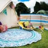 A white canvas tent next to a striped windbreak panel and a blue rug, surrounded by a sunlounger and toys