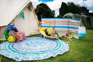 A white canvas tent next to a striped windbreak panel and a blue rug, surrounded by a sunlounger and toys
