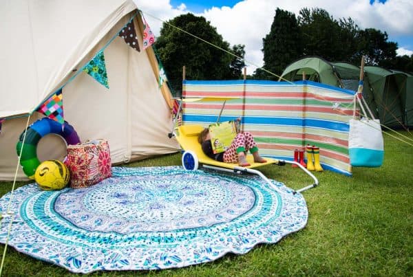 A white canvas tent next to a striped windbreak panel and a blue rug, surrounded by a sunlounger and toys