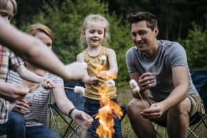 Three children, one man and a woman toast marshmallows around a campfire flame