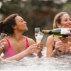 Group of women drink champagne and laugh in a hot tub.