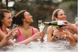 Group of women drink champagne and laugh in a hot tub.