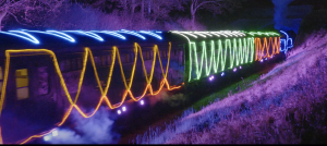 A steam train travels through the mist, covered in multicoloured Christmas lights.